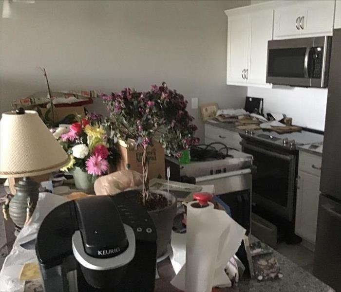 Kitchen countertop is filled with items after a water damage.  Coffee pot, lamp, flowers, and more are laying on the counter