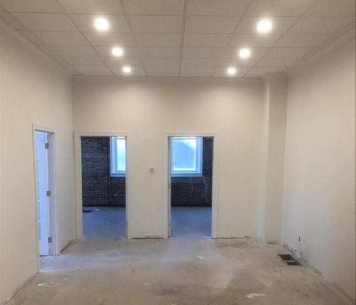 Room with three doorways and white walls with drop ceiling with 6 lights