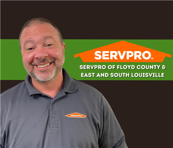 man smiling at camera with a dark background and a SERVPRO logo on the wall