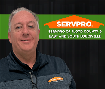 A man in a SERVPRO shirt smiling at the camera with a black backdrop and a SERVPRO logo