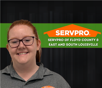 woman with red hair smiling at the camera with dark background and SERVPRO logo on the wall