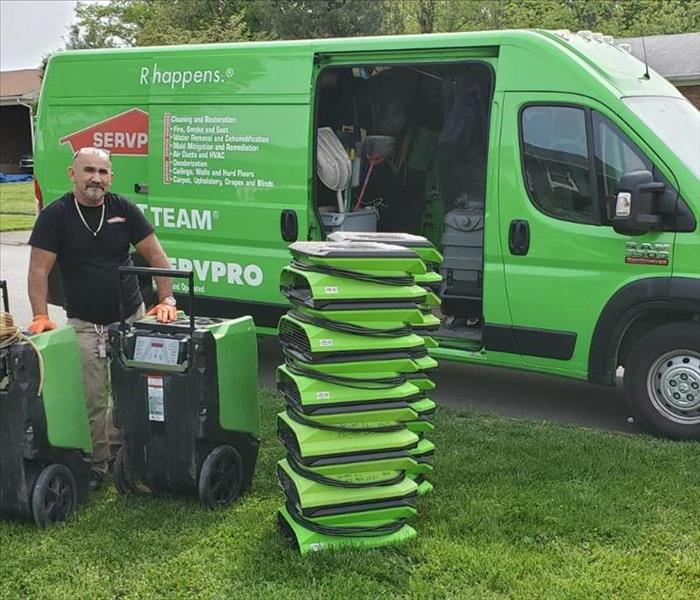 Green SERVPRO van with employee loading air movers that are stacked on the grass.