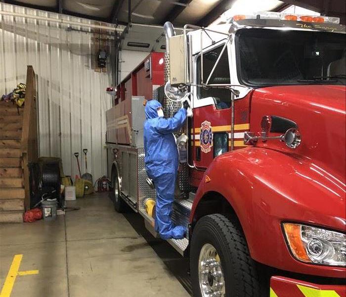 SERVPRO employee wearing a blue PPE suit and rag cleaning an EMS vehicle for a proactive cleaning