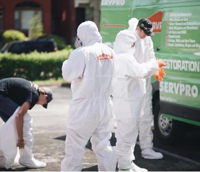 Three SERVPRO employees putting on white PPE suites standing in front of a green van