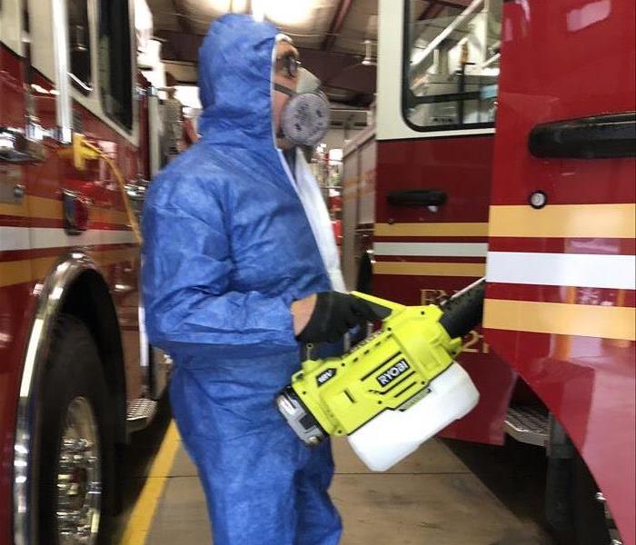 SERVPRO employee wearing a blue PPE suit fogging a firetruck to for a proactive virus cleaning